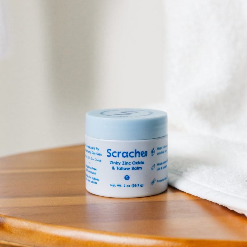 Jar of Scracher balm on a wooden surface with a white towel in the background